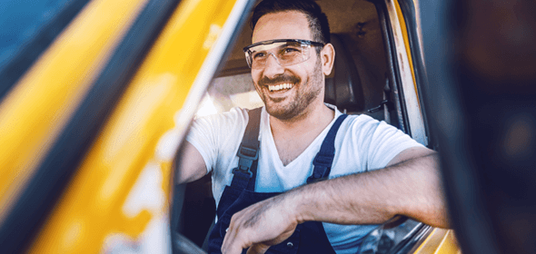 A man wearing work goggles, smiling while driving a truck.